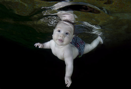 5 Months Infant Boy Learning To Swim Underwater In The Swimming Pool On Black Background. Healthy Family Lifestyle And Children Water Sports Activity. Child Development, Disease Prevention