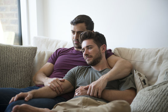 Gay Male Couple Relax On Sofa Watching TV 