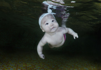 6 months infant girl learning to swim underwater in the swimming pool on black background. Healthy family lifestyle and children water sports activity. Child development, disease prevention