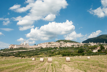 Panoramic view of the ancient town of Assisi with dramatic cloudscape, golden hay bales, Umbria,...