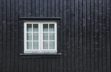 White casement window with mullions, and blinds on the inside, fastened in a black board and batten wood wall