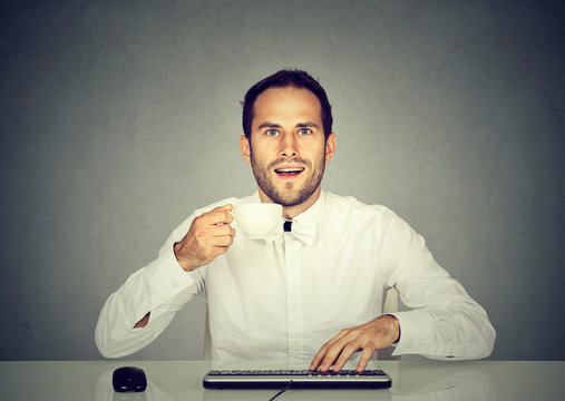 Amazed man using computer holding cup of coffee.