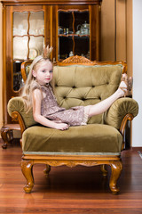 little girl blond hair wearing crown standing at the chair