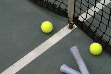 tennis balls, racket grip and net on hard court