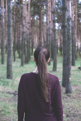 A girl stands with his back in the woods