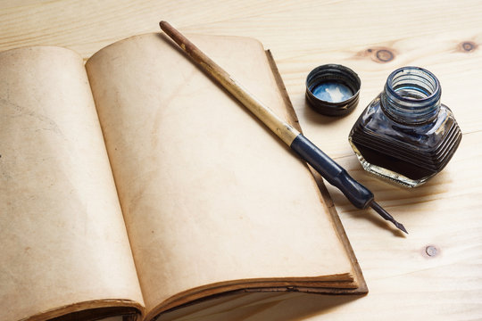 still life photography : quill pen with inkwell and opening old book on pine wood table