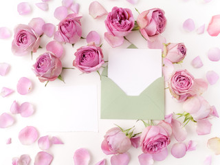 Paper envelop with white card and pink roses. Flat lay, top view