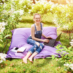 Obraz premium Freelancer working in the garden. Writing, surfing in the internet. Young woman relaxing and having fun in park area. Distance education, freelance concept.