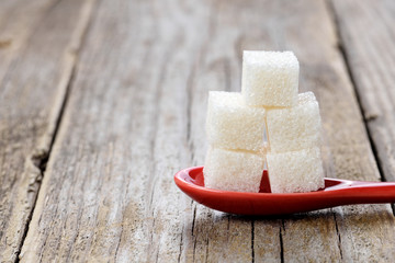 White sugar cubes in spoon on wooden background