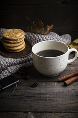 Cup of coffee/tea, cookies, fallen leaves, earphones, and scarf on wooden table.