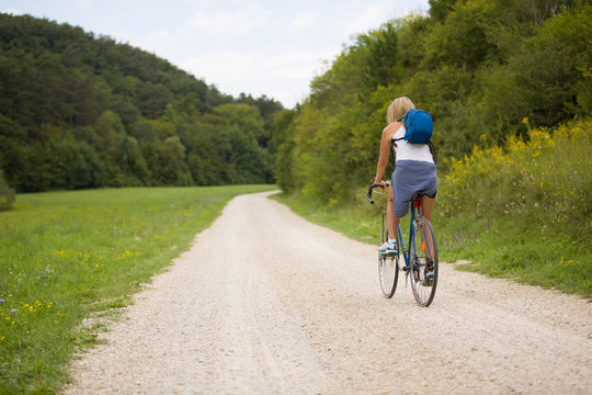 Blonde woman ride bicycle outdoor, next to a forest