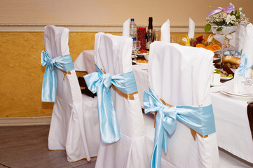 Wedding hall decoration. Chairs in a white case with blue ribbons
