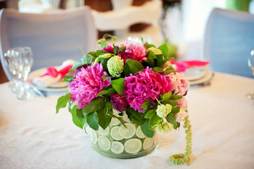 Wedding table decoration, transparent vase with sliced citrus, pink peonies against the white tablecloth. Floral