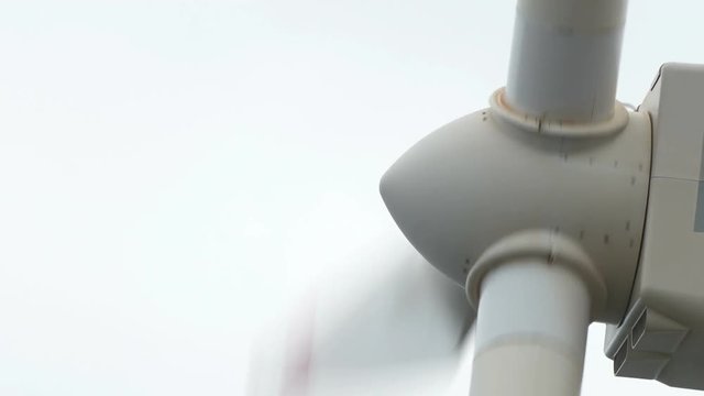 Close-up the shaft the blades of a wind turbine, rotating on a cloudy day.