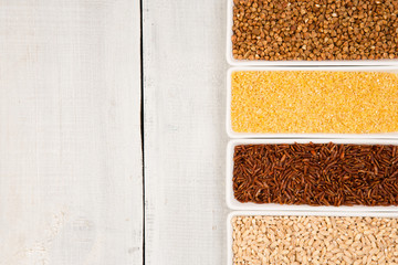 Various groats in bowls on white wooden table