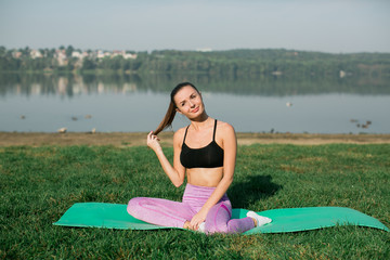 Young woman doing yoga in morning park near lake 