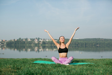 Young woman doing yoga in morning park near lake 