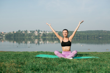 Fototapeta na wymiar Young woman doing yoga in morning park near lake 