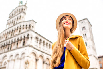 Young female traveler in yellow sweater and hat standing in front of San Michele basilica in Lucca old town in Italy. Having great vacations in Lucca - obrazy, fototapety, plakaty