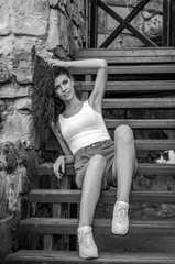 Young charming leggy girl with curly hair in a white shirt and red shorts sitting on the wooden stairs near the fortress in Lviv during a walk on a warm summer sunny day