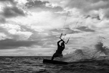 rider on kite between water and cloudy sky.