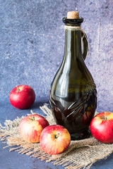 Apple vinegar.   Bottle with apple vinegar and apples on the burlap on a blue background.