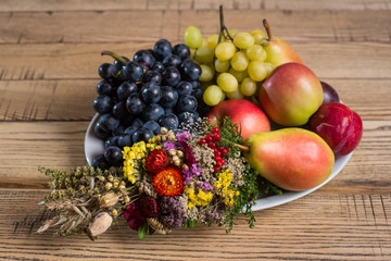 Close-up of fruit plate with wild flower decorations on the wood table. White and black grapes, apples, pears, plums on the platter