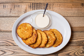 Potato pancakes served on white plate with sour creamon a white plate at the rustic wooden background. Close-up