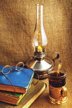 Kerosene lamp old book and glasses on a background of jute