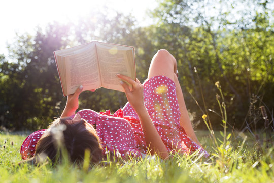 Young girl reading a book outside in nature.