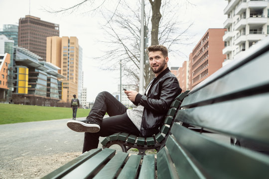 Gesch&auml;ftsmann mit Smartphone sitzt auf einer Parkbank