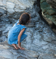 Petite fille sur un rocher penchée au dessus de l'eau
