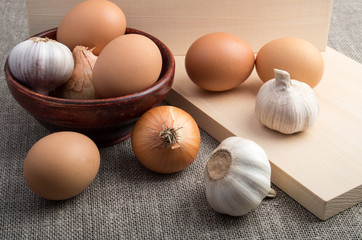 Eggs, onions and garlic next to an old wooden bowl