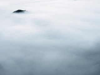 Dark peak of hill  sticking out from heavy fog. Deep misty valley full of creamy mist