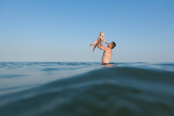 Young dad in the sea playing with his little daughter. He throws up her