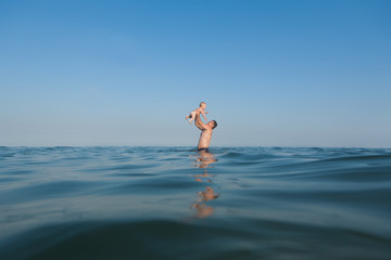 Dad is in the water in the sea, and throws up baby girl