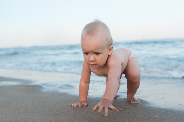 Fototapeta na wymiar Baby blond girl crawling on a sandy beach