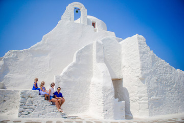 Family vacation in Europe. Parents and kids sitting on the stairs of Paraportiani church on Mykonos Island, in Greece