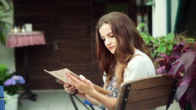 Pretty, romantic girl sitting on the wooden chair in the cafe and reading menu
