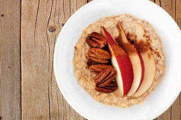 Breakfast oatmeal with red pear, pecans and cinnamon, close up on rustic wood