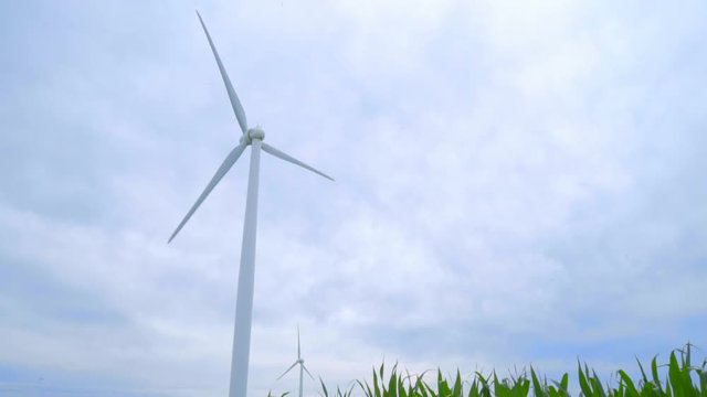 Wind power generator against cloudy sky. Wind turbine against sky. Dolly shot of wind generator against sky. Renewable energy resource. Wind power concept. Wind turbine generating electricity