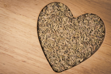 Fennel dill seeds heart shaped on wooden board