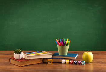 School items on desk with empty chalkboard