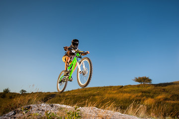 Fototapeta na wymiar Biker riding downhill and making extreme jump on a mountain bike on the hill against blue sky. Wide angle view