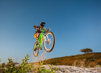 Fototapeta na wymiar Athlete bicyclist in helmet and glasses jumping on a mountain bike on the mountain against blue sky. Wide angle view