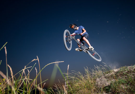 Male biker flying on a mountain bike against evening sky in the mountains. Cyclist is wearing sportswear helmet and glasses. Bottom view. Extreme cycling.