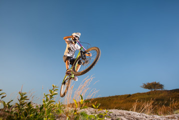 Fototapeta na wymiar Cyclist flying on a mountain bike against blue sky in the mountains. Cyclist is wearing sportswear white helmet and glasses. Wide angle view. Dangerous freeride