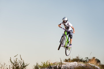 Male cyclist flying on a mountain bike over the top of the mountain against blue sky. Downhill cycling. Extreme sport