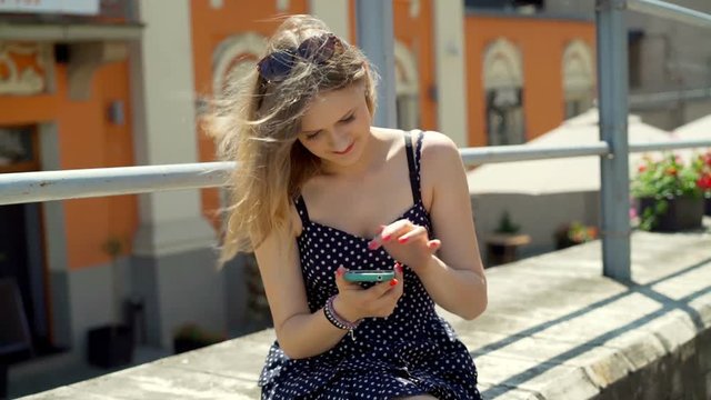 Pretty girl sitting in the city and typing messages on smartphone
