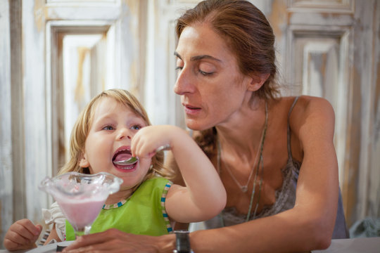little child eating ice cream with mother at restaurant